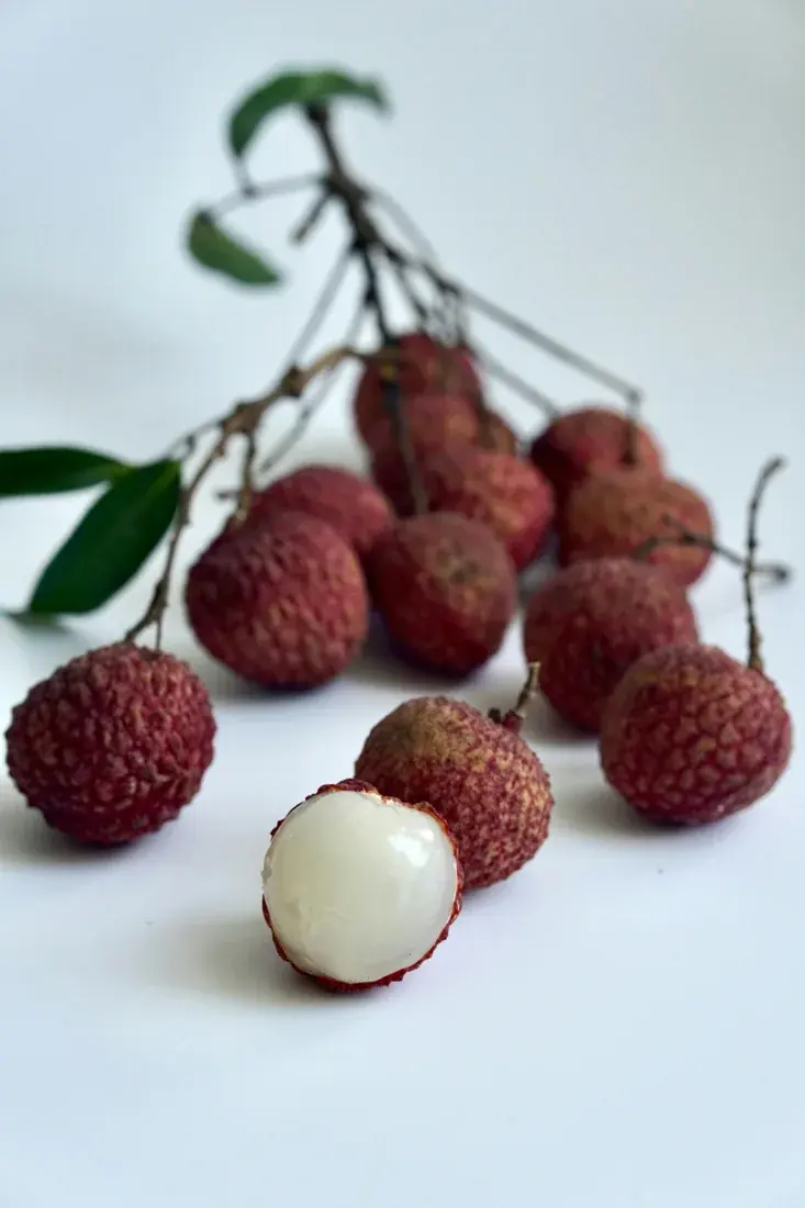 A bunch of red litchis with one peeled fruit showing white flesh.