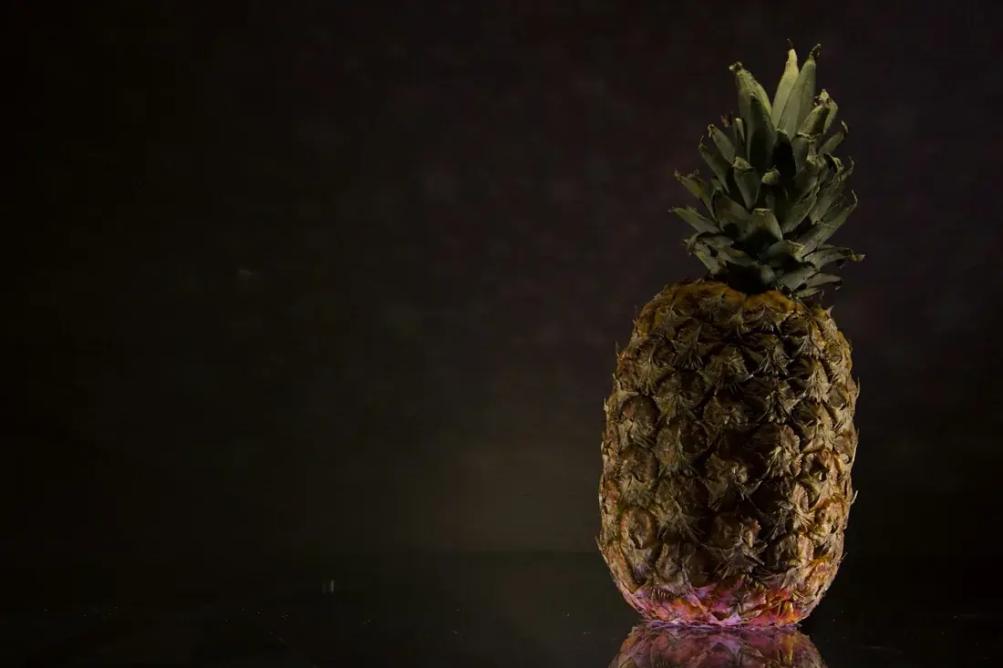 Whole pineapple fruit with green crown against a dark background.