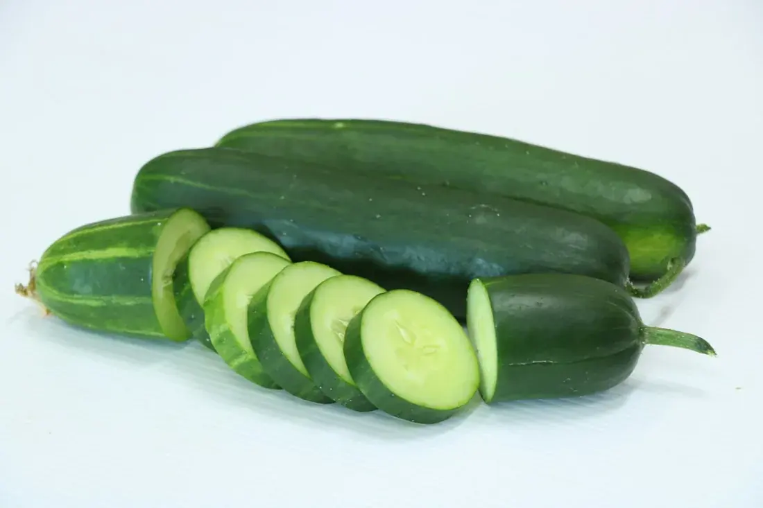 Fresh whole cucumbers and cucumber slices on a white surface